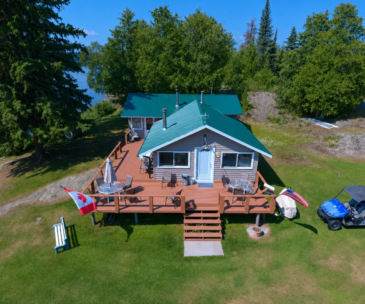 The green-roofed lodge and its wraparound deck at Wilderness Fishing Oasis